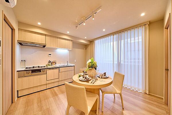 木目調の扉を採用したシステムキッチンを備えた室内には、ダウンライトやダクトレール照明が設置されているほか、バルコニーへ繋がる大きな掃き出し窓が配置されています。