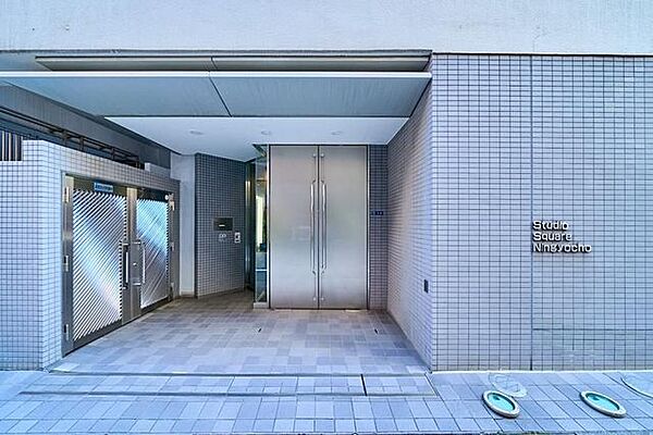 グレー系のタイルで仕上げられた外壁と床面が印象的なエントランスには庇が設けられており、奥には両開きの金属製扉が備えられたフラットで出入りしやすい構造となっています。