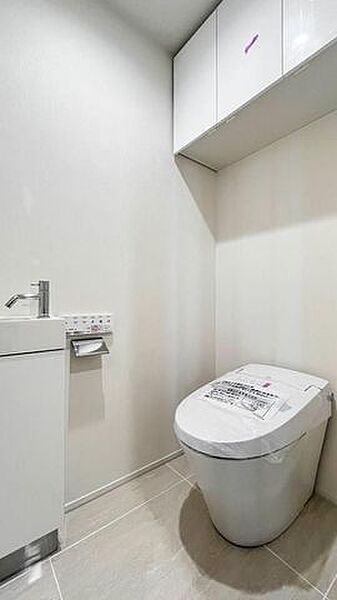 白を基調とした清潔感のあるトイレには、すっきりとした印象のタンクレストイレをはじめ、独立した手洗い器や備品等を整理して収納できる上部吊戸棚が備わっています。
