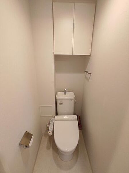 温水洗浄便座完備の清潔感あるトイレ。上部には吊戸棚があり、掃除用具等もスッキリ収まります。