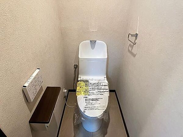 白い最新式のトイレ。横に棚があり、トイレットペーパーホルダーやタオル掛けも完備。