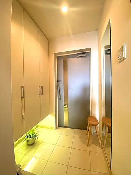 【玄関】全身鏡や玄関タイル保護シートが設置されております。玄関収納は、下部が開放されたウォールタイプで、天井の高さまで収納のため、収納力があります。