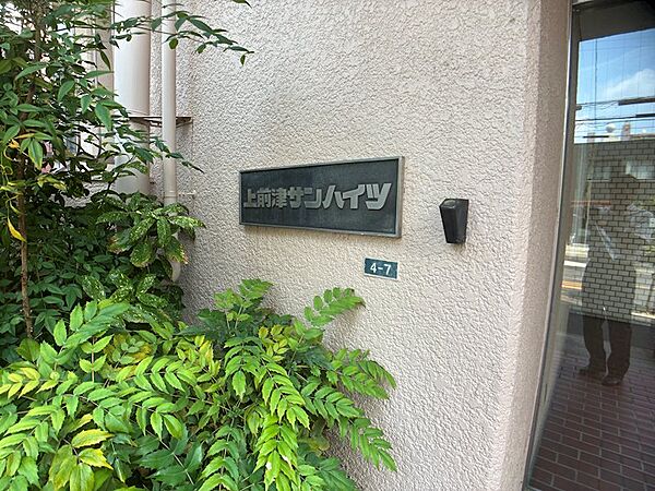 「上前津サンハイツ」の看板と、建物の壁面です。緑豊かな植栽が、落ち着いた雰囲気を演出しています。