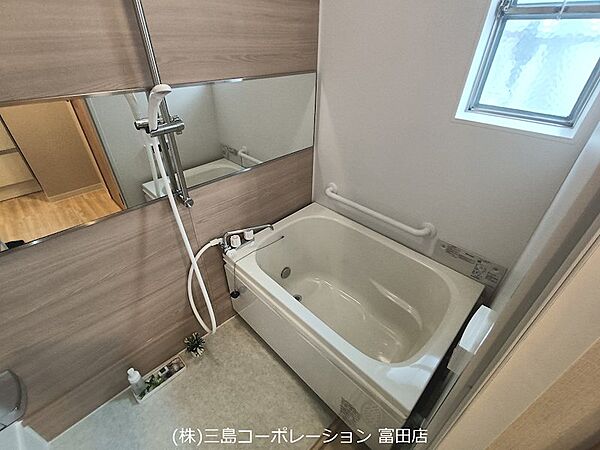 木目調の壁が温かみを感じさせる浴室。採光窓付きで、明るく快適なバスタイムを過ごせます。手すりも備わり、安心してご利用いただけます。