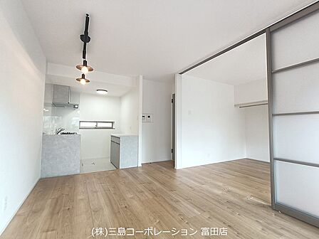 明るい木目調の床と白い壁が調和したリビング。奥には使い勝手の良いキッチンと、空間を仕切れるスライドドアが設けられています。