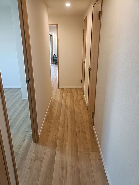 明るい木目調のフローリングが特徴の廊下です。各部屋へ繋がる扉も同系色で統一され、すっきりとした印象を与えます。