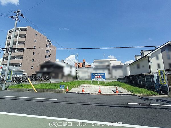 青空が広がる開放的な現地。周辺にはマンションや商業施設が点在し、生活利便性が期待できる環境です。
