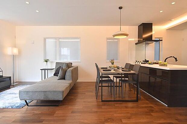 【モデルハウス/LDK】木目が美しいブラウンカラーのフローリングが印象的なLDK。落ち着きと温もりを感じられるデザインです。家具のような佇まいのオープンキッチンが、空間の印象を引き締めてくれます。