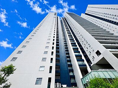 外観：爽やかな青空の下に贅沢なほどに降り注ぐ陽光、豊かな居住性。クオリティが見事に調和した住空間。（空の加工を生成AIで行っています）