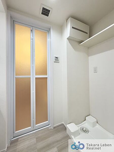 洗濯機置場。収納棚が設置されている為、洗剤類の収納場所としてお使いいただけます。
