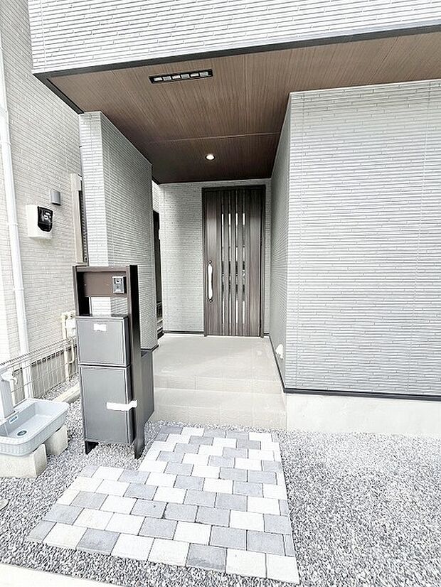 洗練された色合いの外壁と木目調の天井が調和する落ち着いた佇まいの玄関アプローチ