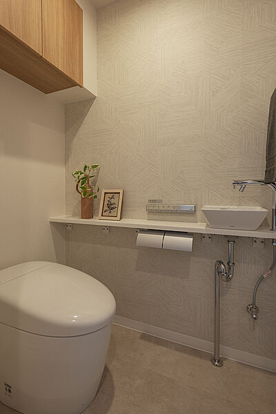 【トイレ】スタイリッシュなデザインが魅力的な、温水洗浄便座付きのトイレです。独立した手洗い器を設置しているため、使用後すぐに手洗いができます。収納に便利な吊戸棚付きです。