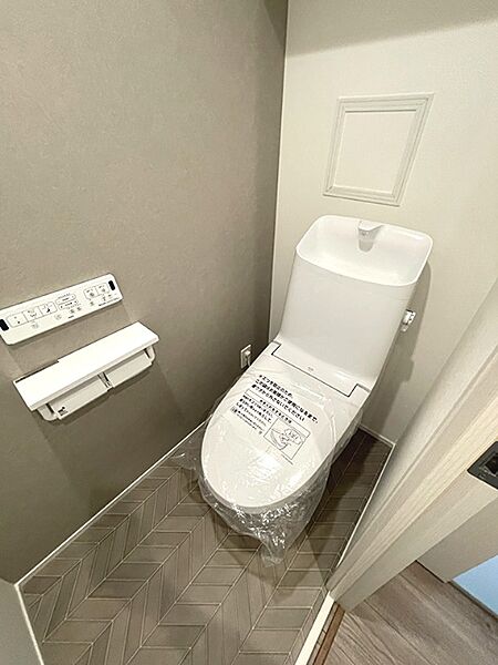 清潔感のあるトイレ空間。落ち着いた色合いの壁とヘリンボーン柄の床が、心地よい時間を提供します。