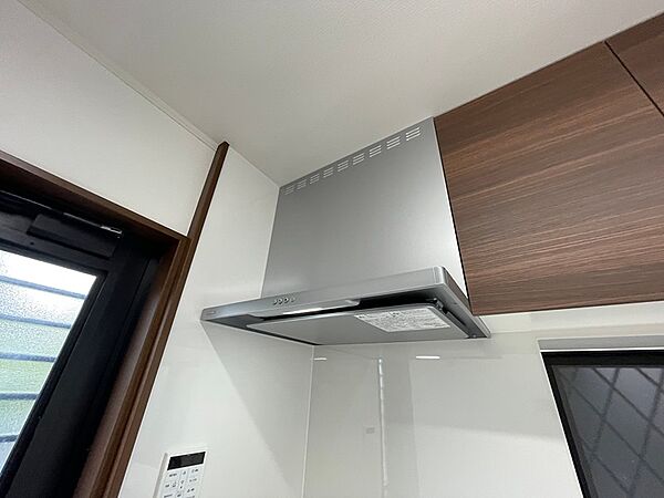 すっきりとしたデザインのレンジフードと、木の温もりを感じる吊戸棚が調和したキッチン。窓からの採光も良く、明るい空間で料理を楽しめます。