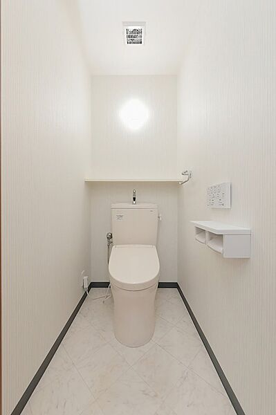 清潔感のある白を基調としたトイレは、壁のアクセントクロスが心地よい空間を演出します。収納棚も備え、機能性も兼ね備えています。