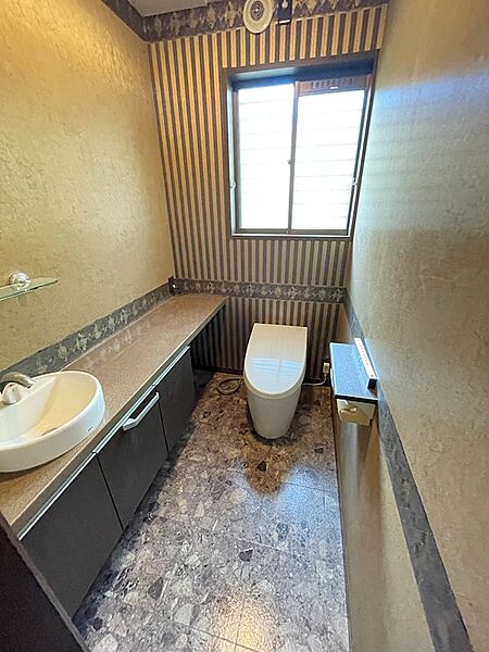 個性的なアクセントクロスが印象的なトイレ空間。手洗いカウンター下の収納で、すっきりとした空間を保てます。窓から光が差し込み、換気も良好です。