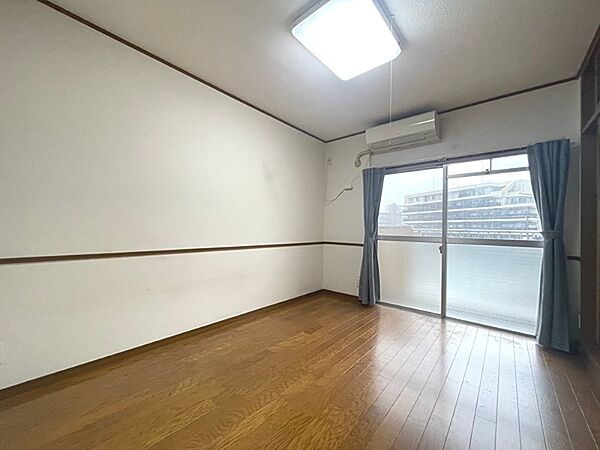 白を基調とした壁に木目調のフローリングが映える居室です。バルコニーに面した窓から光が差し込み、明るい空間を演出します。