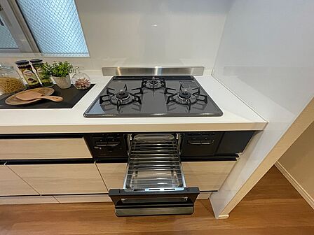 3口コンロとグリルを備えたキッチンは、料理の幅を広げます。収納も充実しており、調理器具や食器をすっきりと整理できます。