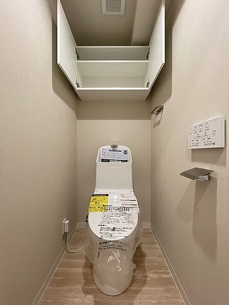 清潔感のある白いトイレ空間です。上部の収納棚には、トイレットペーパーや清掃用品などをすっきりと収納できます。快適な毎日をサポートする設備が整っています。