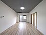 リビング/ダイニング：天井のダウンライトとグレーのアクセントクロスが洗練された空間を演出。明るいフローリングと白い壁が、お好みの家具を惹きたてます。広々としたリビングで、あなたらしい暮らしを始めてみませんか。