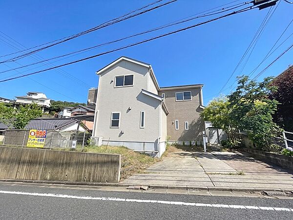 青空が広がる現地写真です。周辺には住宅が立ち並び、閑静な環境がうかがえます。駐車場スペースも確保されています。