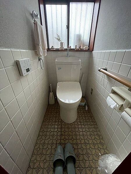 窓から光が差し込む明るいトイレ空間。手洗い付きの便器で節水にも配慮。手すりも設置され、安心してお使いいただけます。