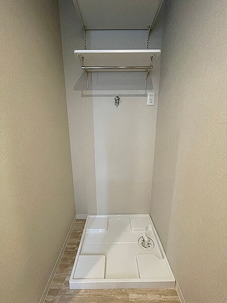 洗濯機パンが設置された洗面所です。上部には棚とハンガーパイプがあり、洗剤やタオルなどの収納に便利です。