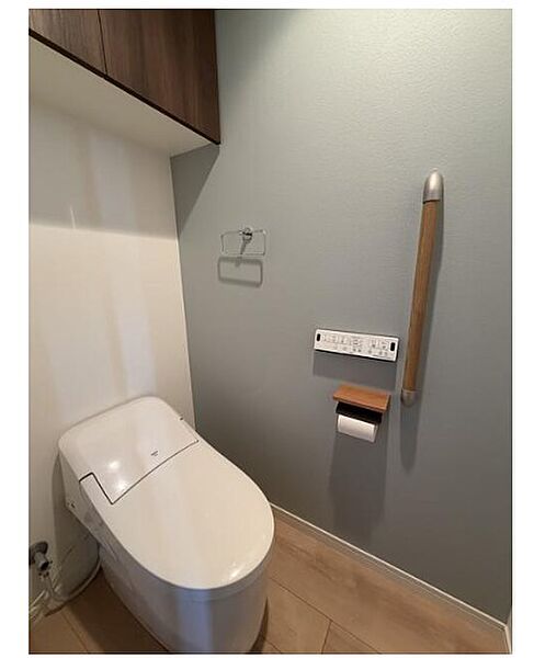 落ち着いた色合いの壁紙が印象的なトイレ空間。手すりや上部収納も備わり、快適さと機能性を兼ね備えています。