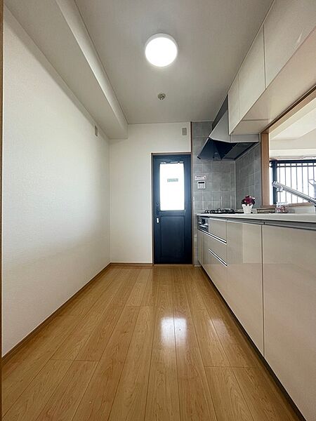 明るい木目調のフロアと清潔感のある白いキッチン。勝手口もあり、家事のしやすいレイアウトです。