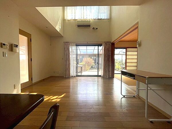 明るい陽光が降り注ぐ、開放的なリビングです。高い天井が空間に広がりと心地よさをもたらし、ウッドデッキへと繋がる窓が開放感を演出します。