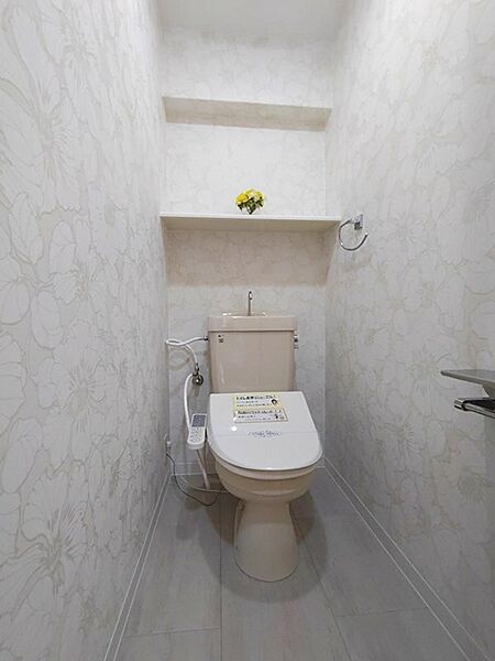 落ち着いた花柄の壁紙が心地よい空間を演出。上部には便利な棚を設け、トイレットペーパーのストックや小物の収納に役立ちます。清潔感のある温水洗浄便座で、毎日を快適に。