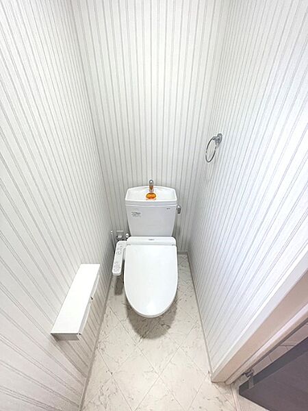 清潔感のあるストライプのクロスとマーブル模様の床が特徴のトイレ空間。ウォシュレット付きで、快適な毎日をサポートします。飾り棚やタオルリングも完備。