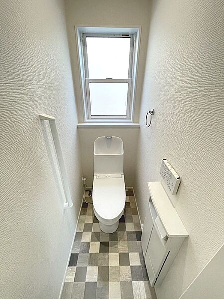 窓があり、明るい印象のトイレ空間。アクセントとなるチェック柄の床が清潔感を演出します。収納も備え、すっきりとした使用が可能です。
