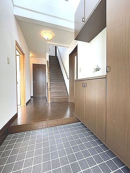 広々とした玄関は、明るい照明と木目調の収納が調和し、居住者様を温かく迎え入れます。上部まである収納は、玄関をすっきりと保ちます。