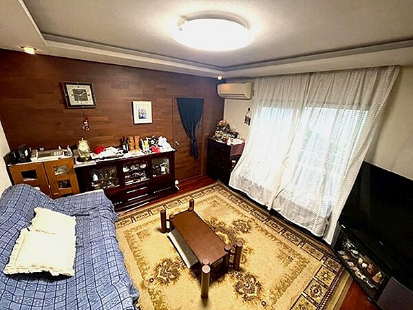木目調の壁が落ち着いた雰囲気を醸し出すリビング。日中はレースカーテンから柔らかな光が差し込み、家族団らんのひとときを彩ります。お気に入りの家具を配置して、自分らしい空間を創造してみてはいかがでしょうか