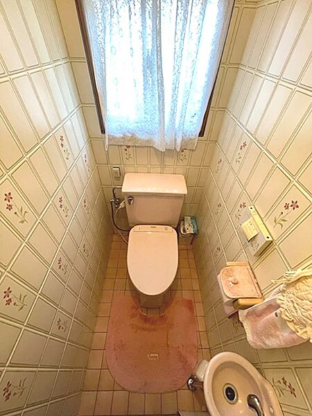 小窓から光が差し込む明るいトイレ空間。清潔感のある便器と温水洗浄便座が備わっています。花柄の壁紙が空間に彩りを添えます。