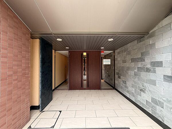 天然石調の壁面と木目のエントランスドアが上質な雰囲気を演出。住まいへ帰る時間にも、心地よい落ち着きを感じられます。