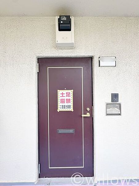 506号室の玄関ポーチ・住戸扉です。施工期間中のため一時的な注意書きを掲示しておりますが、しっかりとした造りの玄関扉とインターホンが設置されており、完成後も安心してお住まいいただけます。