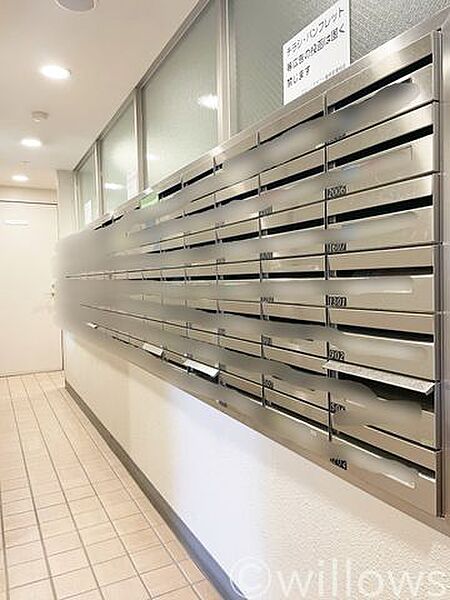 エントランス付近に整然と配置された、使いやすいダイヤル式の集合ポストです。床面や壁面にチラシなどのゴミが見当たらず綺麗に保たれており、タワーマンションならではの行き届いた良好な管理体制が伺えます。