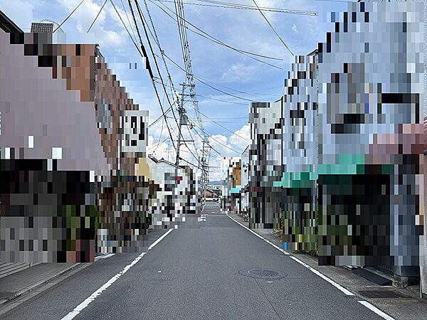 青空が広がる穏やかな日差しの中、現地前面道路です。周辺には店舗や住宅が立ち並び、生活利便性の良い環境です。