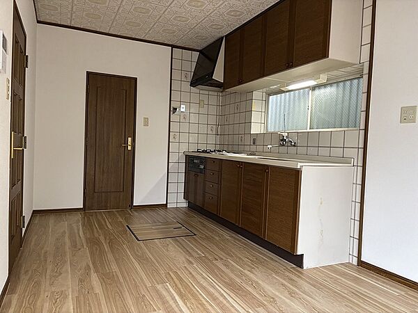木目調の床とシステムキッチンが温かみを感じさせる空間です。窓からの光が差し込み、明るい雰囲気で料理を楽しめます。収納も充実しており、すっきりとしたキッチンを保てます。