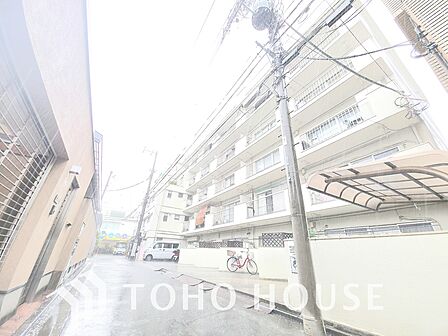 通りに面した、白を基調としたマンションです。1階には飲食店が入っており、にぎやかな雰囲気を醸し出しています。