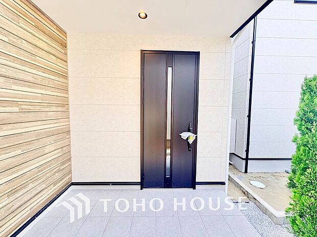 ◆木目調壁が目を惹く玄関ポーチ◆雨の日のお出かけや荷物の搬入時にも便利な深めの軒下設計。ダウンライトが優しく足元を照らし、広々としたタイル敷きスペースがゆとりある暮らしを印象付けます。