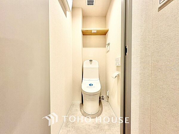 新規交換された温水洗浄便座付きの快適なトイレです。トイレットペーパーや掃除用品の保管に便利な上部固定棚を備え、足元をすっきりと保てます。白を基調とした清潔感あふれるプライベート空間です