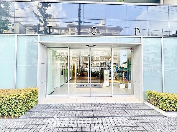 全面ガラス張りの明るく開放的なエントランスアプローチ。上部のシックなダークパネルと両脇の瑞々しい植栽が調和し、居住者や訪れるゲストを洗練された上質な空間へと迎え入れます。