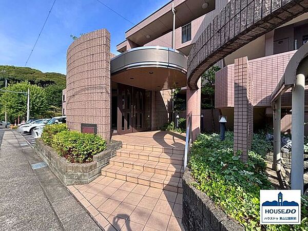 スタイリッシュで重厚感のあるエントランス。緑の植栽が訪れる人々に癒しを与えます。左奥に見えるのは、敷地内平面駐車場です。