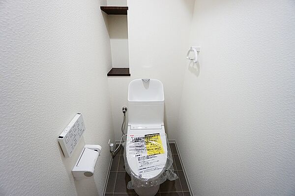 壁リモコンタイプのウォシュレット付き。すっきりした見た目で、トイレ奥の掃除もしやすいです。トイレットペーパーの収納に便利な棚付き。