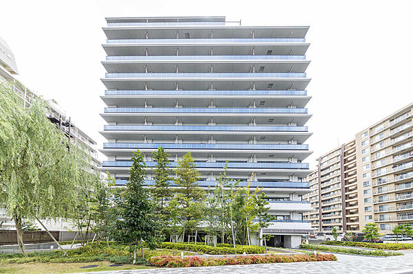 豊かな緑に彩られた敷地内の配棟計画が魅力的な建物全景です。地上13階建ての堂々としたフォルムで、周辺環境と調和しながらも圧倒的な存在感を放つ住まいとなっています。
