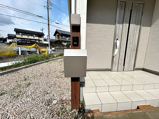 玄関前にはカメラ付インターホンとポストの一体型設備が設置されており、省スペースで玄関まわりがすっきりとまとまります。来訪者の確認や郵便物の受け取りもスムーズに行える、使い勝手の良い玄関まわりです。
