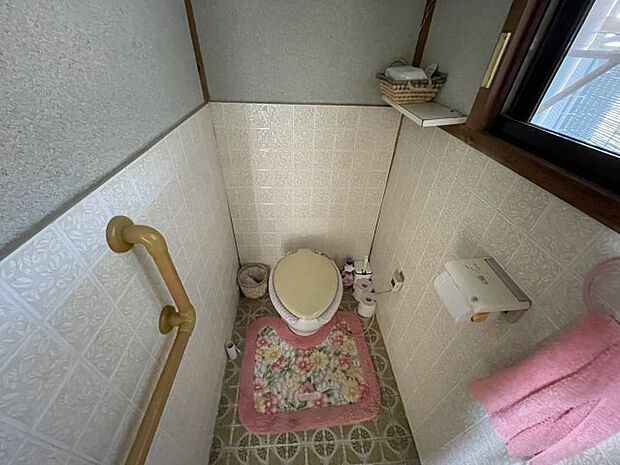 白色の清潔感のあるトイレです。手すりもあり、バリアフリーな作りですね。窓もあるので換気もきちんとできます。ちょっとした物を置いておくのに、上部の棚が便利です。